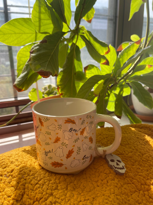 White mug with autumn-themed design on a yellow surface with plants in the background