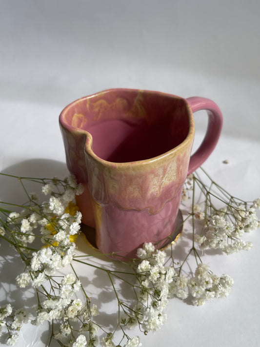 Pink ceramic mug with gold accents on a white background with small white flowers.