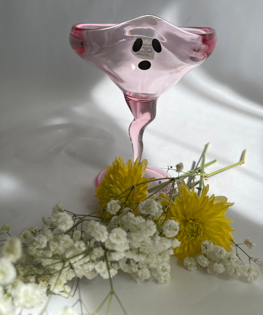 Pink glass object with black dots on a white surface with yellow and white flowers.