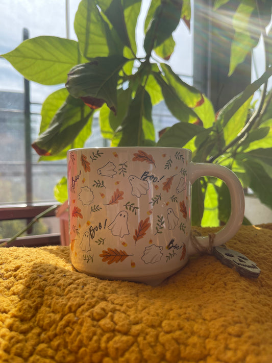 Decorative mug with autumn-themed design on a yellow surface with plants in the background