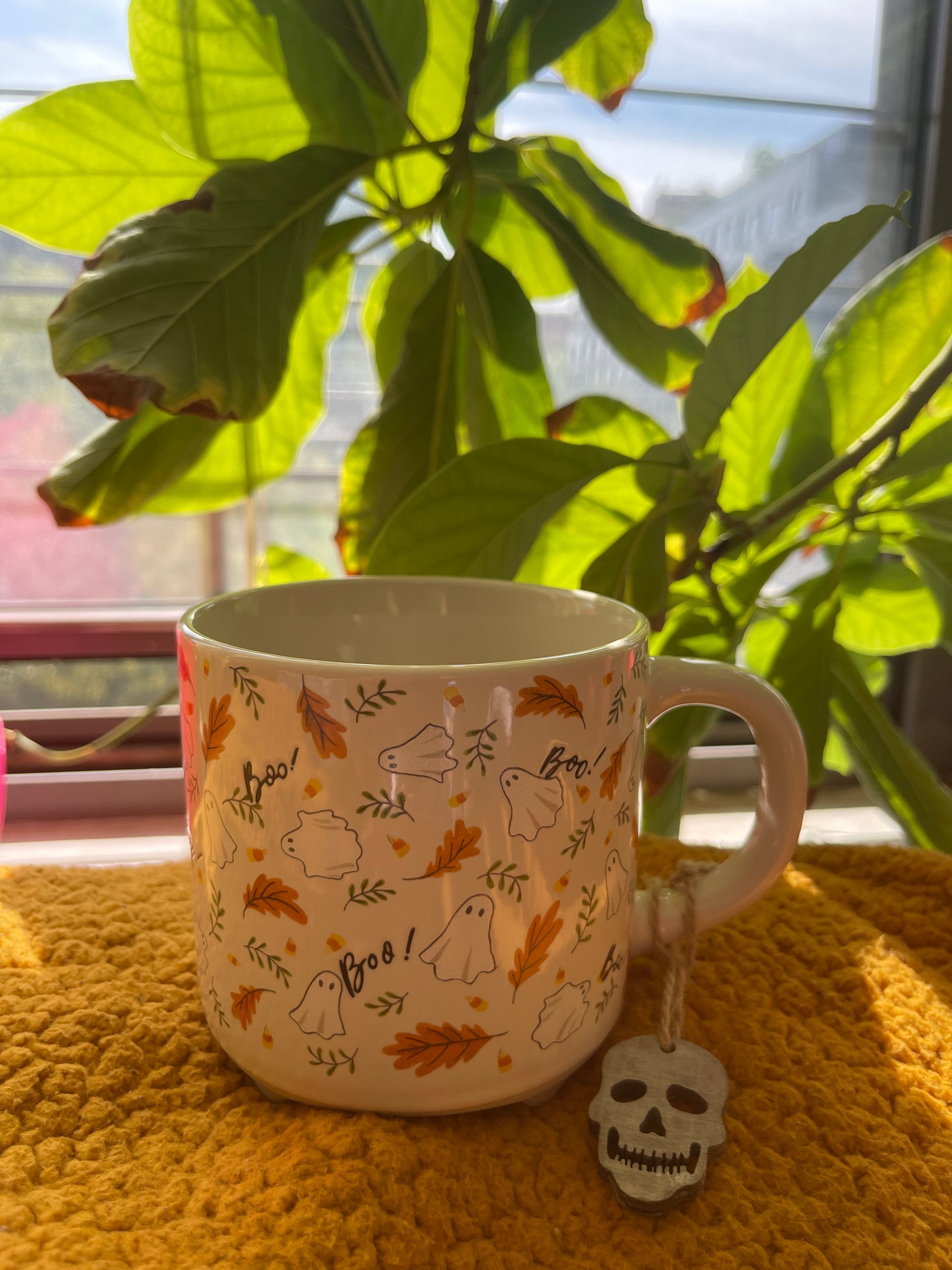 Mug with Halloween-themed design on a yellow surface with green plants in the background