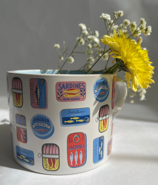 Mug with sardine label designs and a yellow flower on a light background