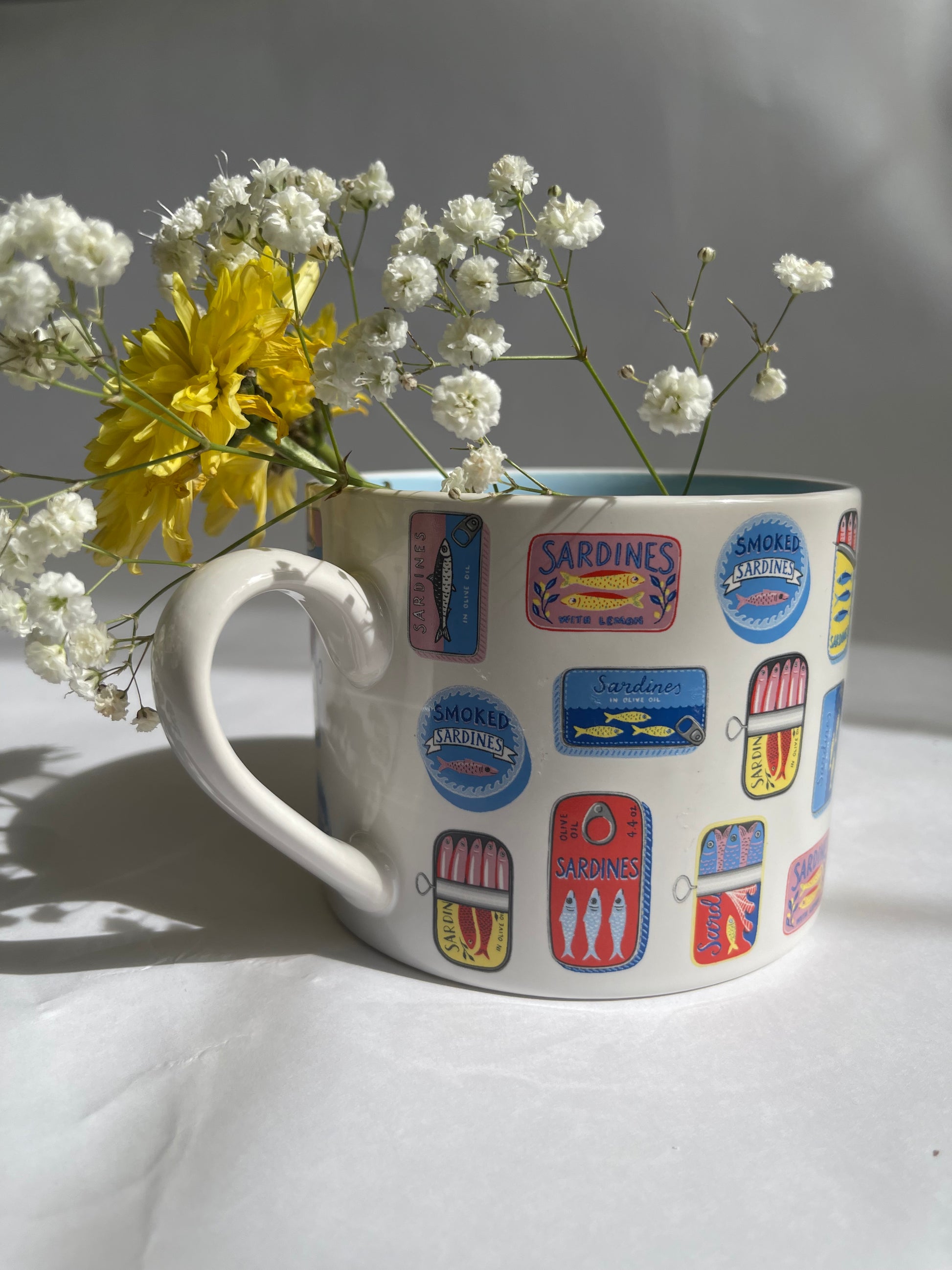 Mug with colorful labels and flowers on a light surface