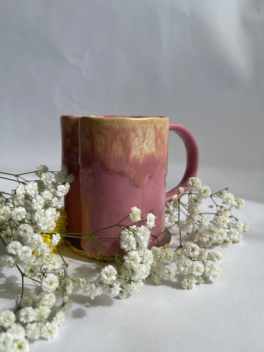 Pink mug with gold interior surrounded by small white flowers on a light background