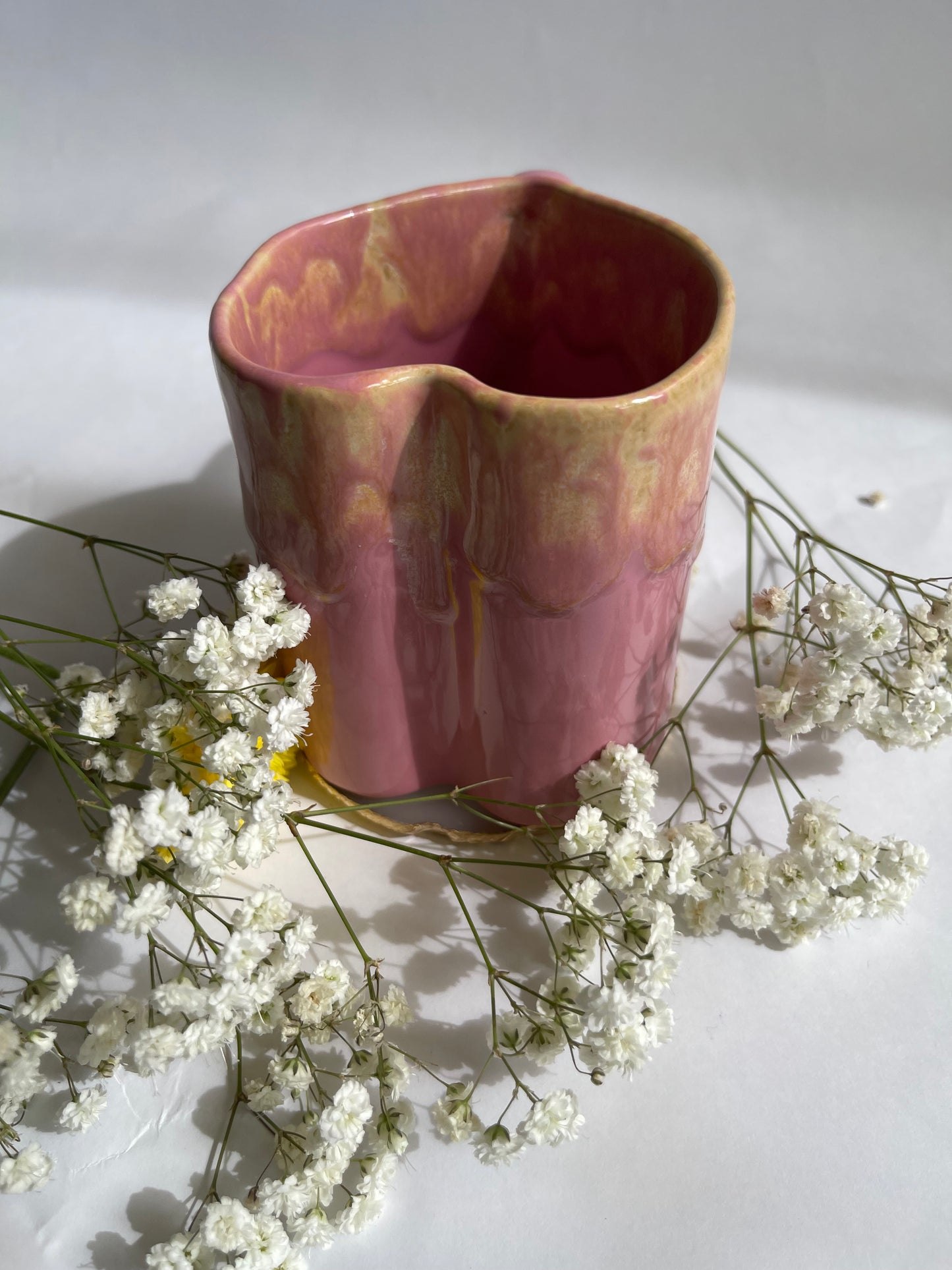 Pink ceramic vase with textured surface on a white background with small white flowers.