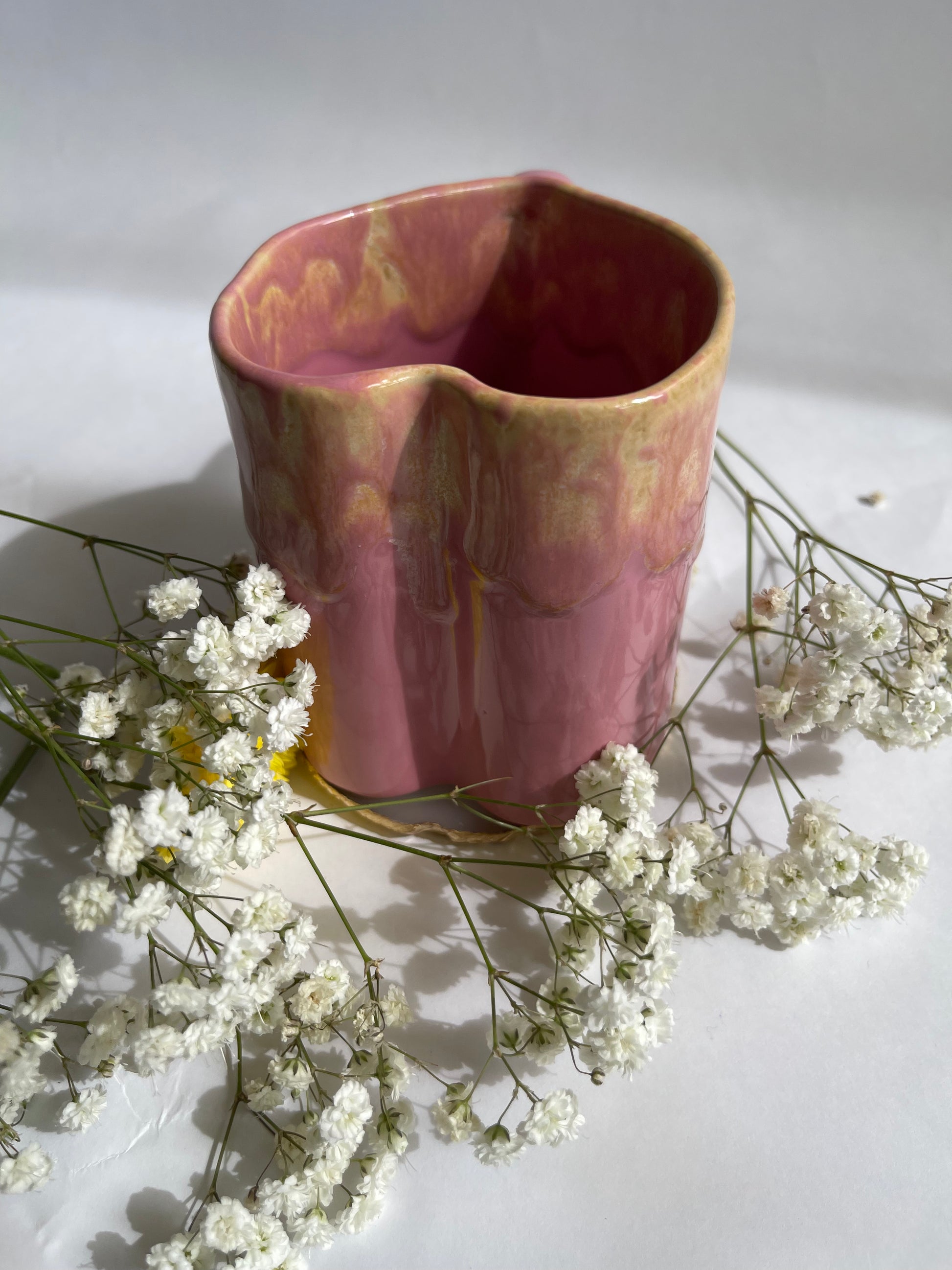 Pink ceramic vase with textured surface on a white background with small white flowers.