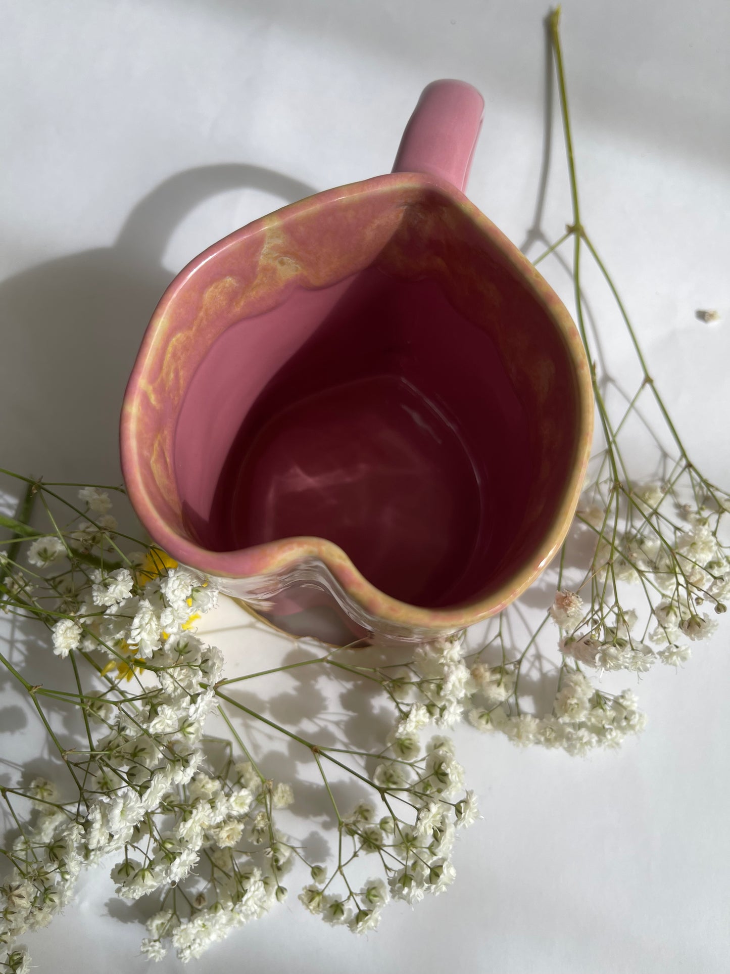 Pink ceramic pitcher with a handle on a white surface with small white flowers around it.
