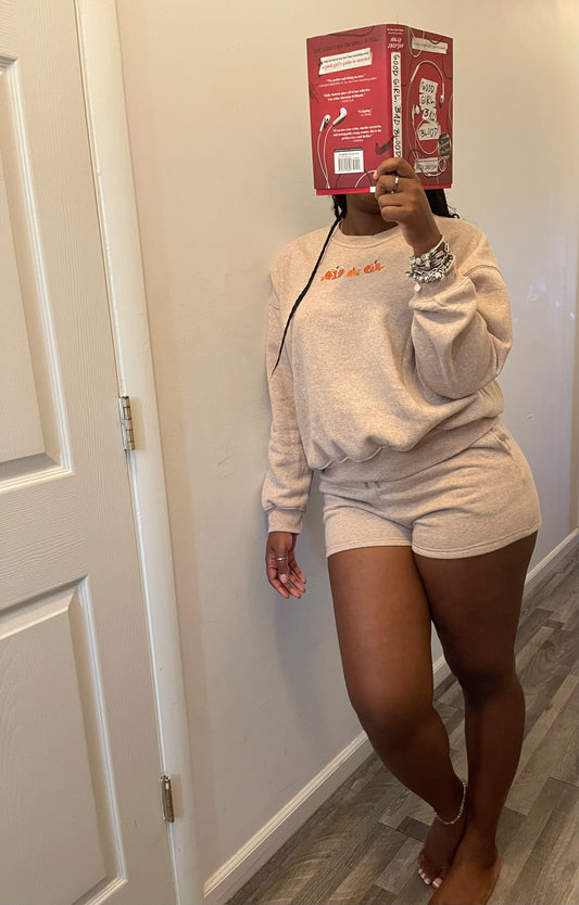 Person wearing a beige sweatshirt and shorts set, holding a red box above their head.