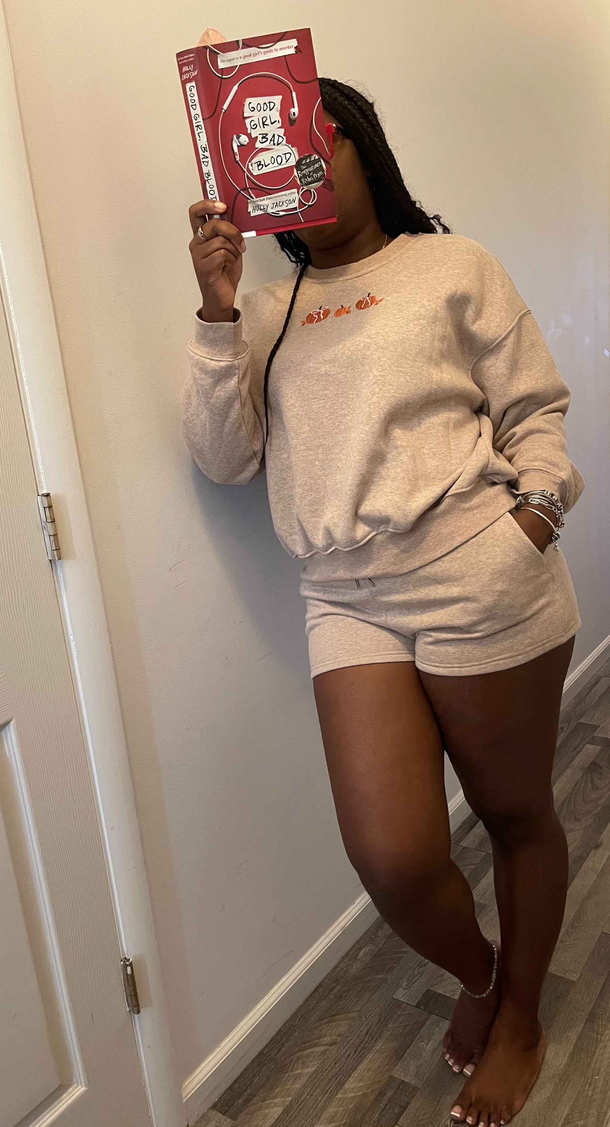 Person wearing a beige sweatshirt and shorts set with a book held over their face.