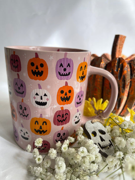 Pink mug with Halloween-themed pumpkins surrounded by white flowers and a wooden basket.