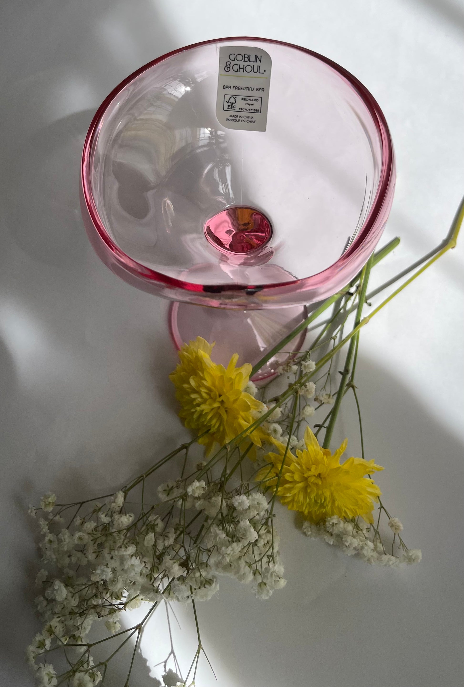 Clear glass with pink rim on a white surface with yellow and white flowers.