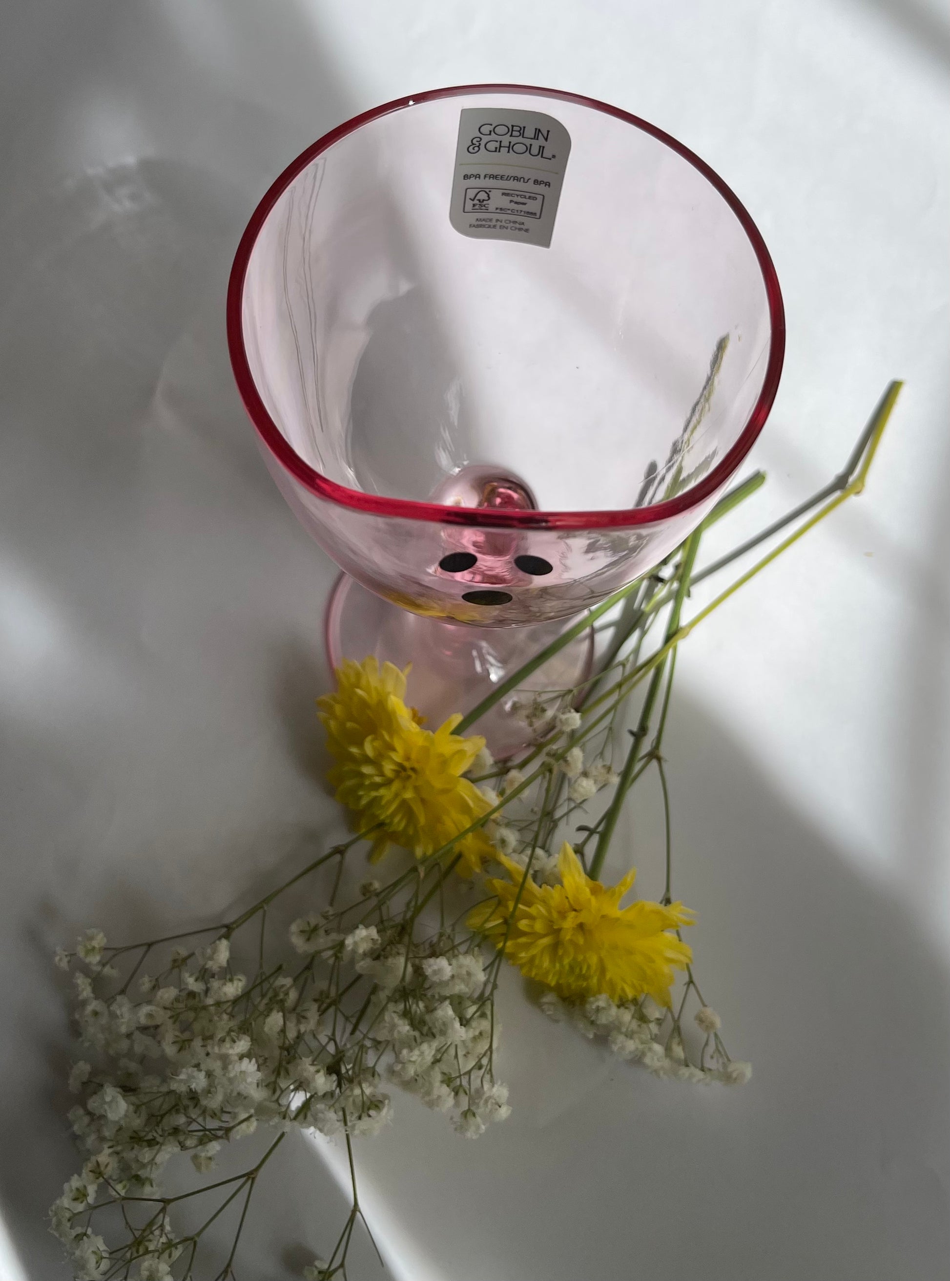 Clear glass vase with red rim containing yellow and white flowers on a white surface
