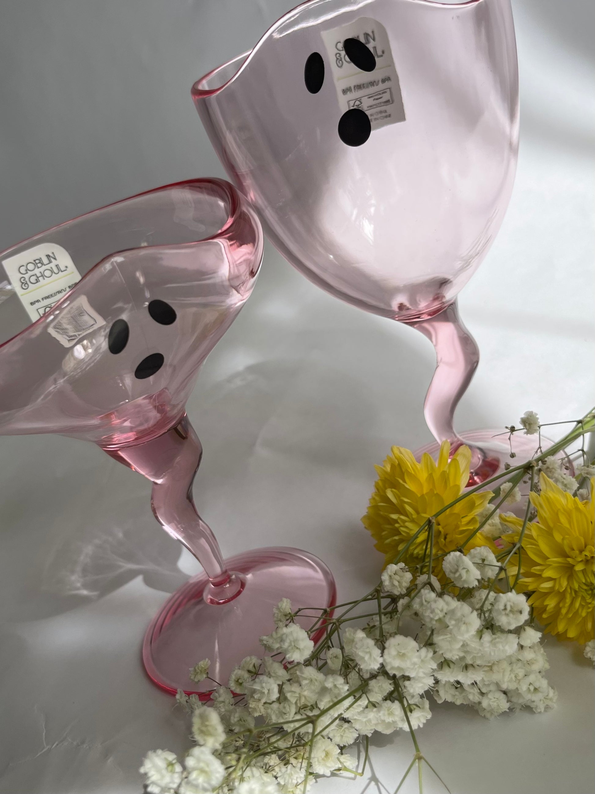 Pink glassware with black dots on a white surface with flowers.