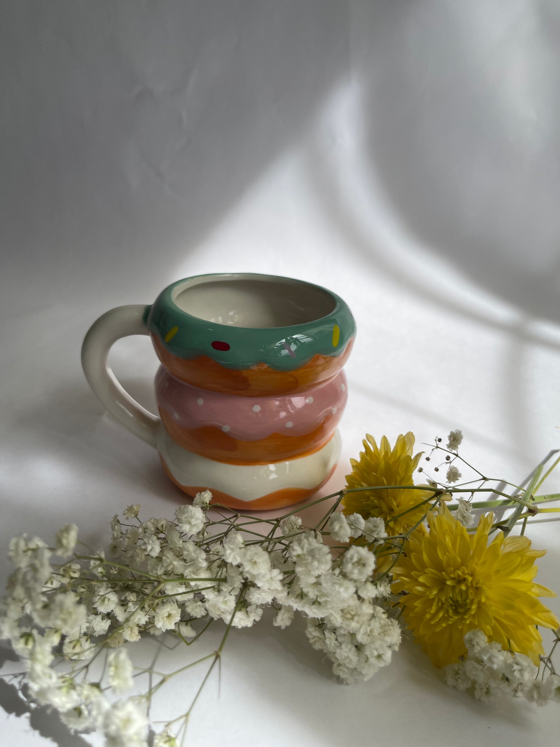 Colorful ceramic mug with a striped design on a white surface with flowers.