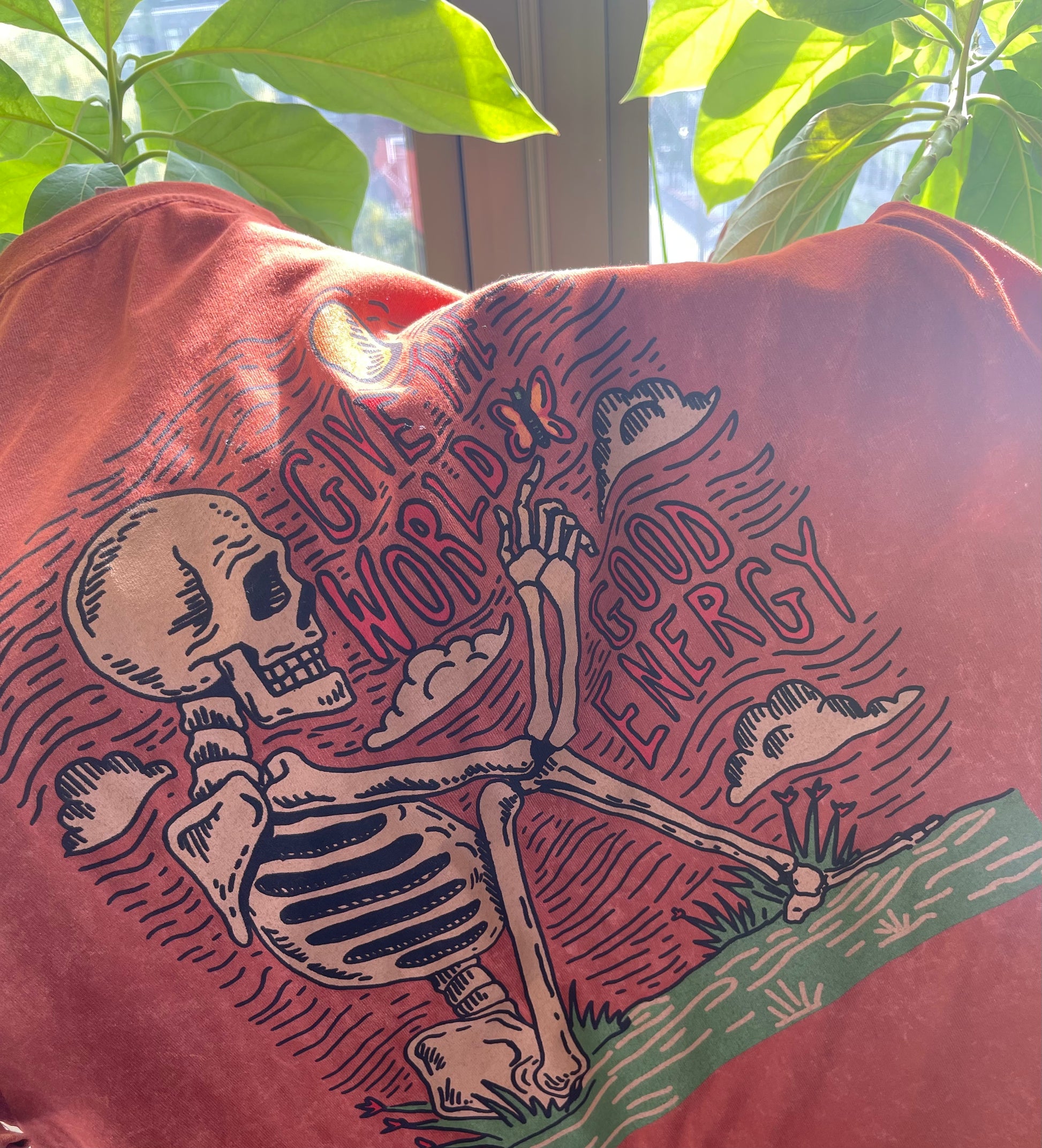 Red t-shirt with a skeleton design and text on a plant-filled background